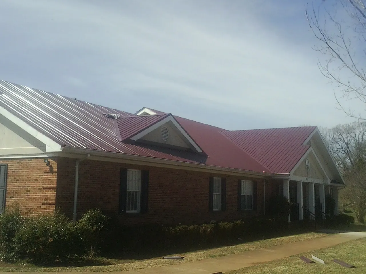 Red metal roof with gabled entries on a long brick building, from a Hail Damage Roof Repair job in Rayville
