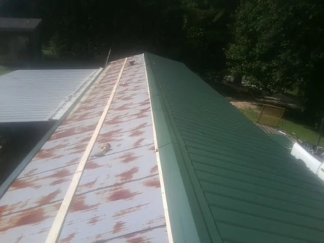 Old rusted panels beside newly installed green metal roofing — Wind Damage Roof Repair by Roofing Brothers in Rayville