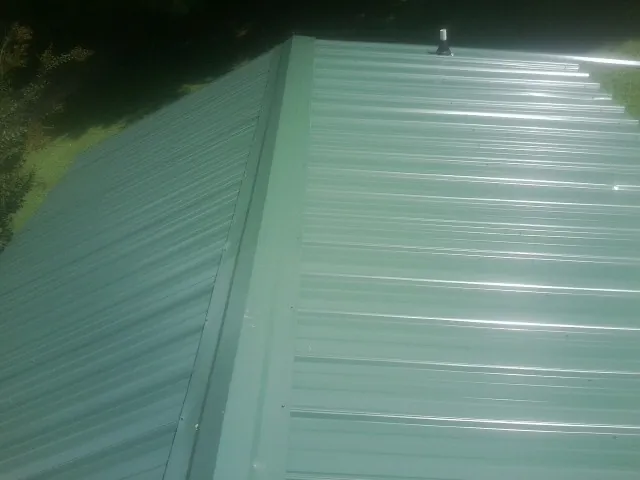 New green metal panels meeting at the ridge of a roof — Flat Roof Repair work by our crew in Rayville