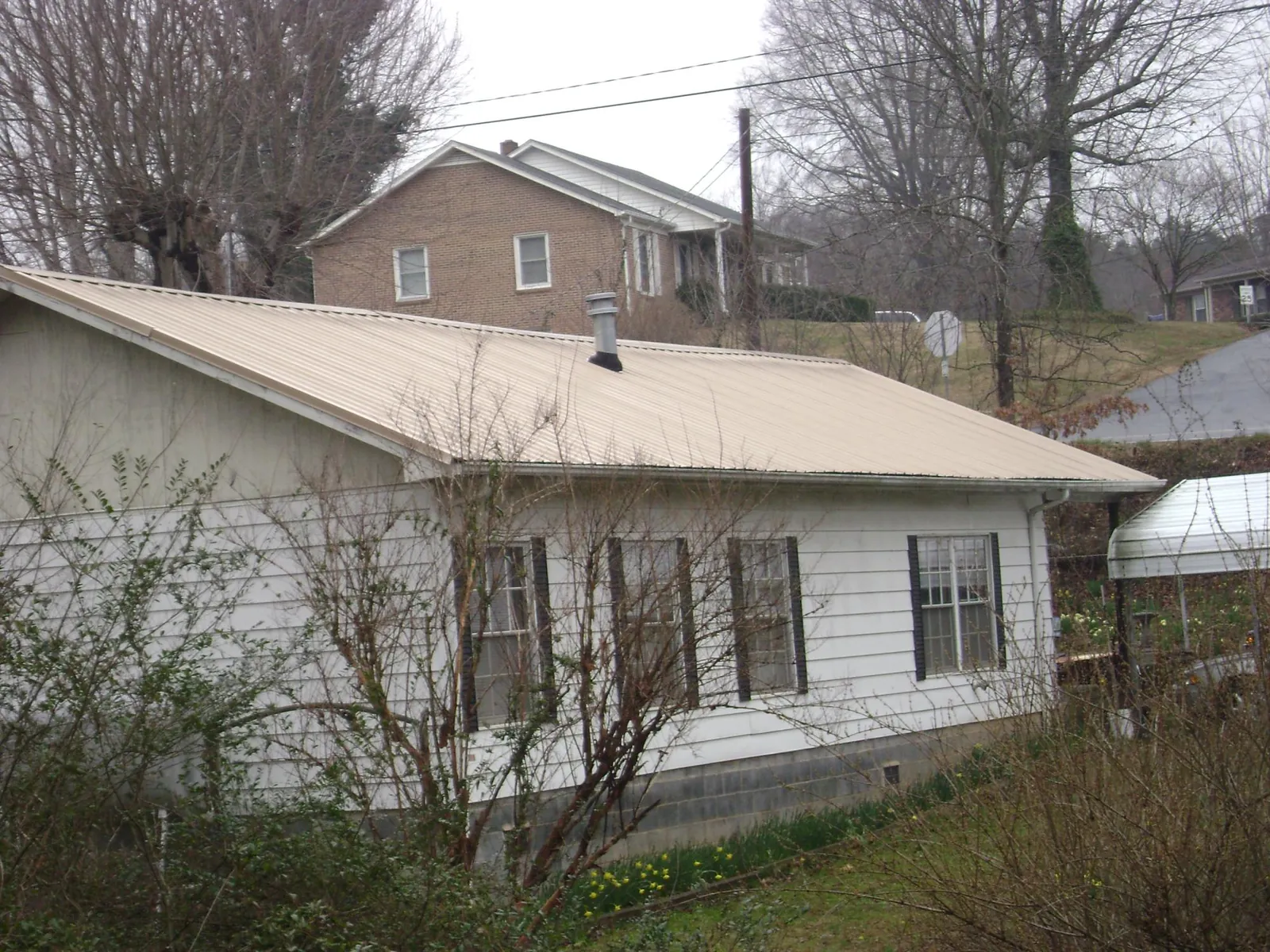 Tan metal roof on a white sided house set into a hillside — Commercial Roofing by Roofing Brothers in Rayville